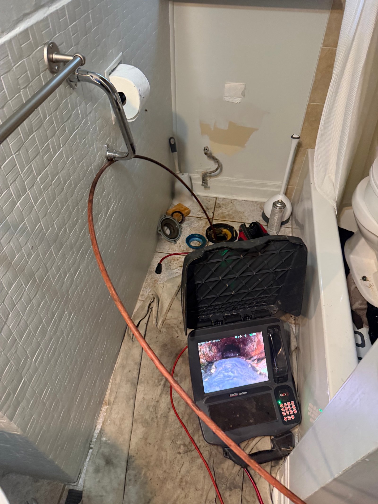 Plumbing technician using a drain snaking machine through a removed toilet flange to clear a main sewer line blockage